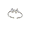 Silver-tone open ring with a sparkling bow centerpiece and leaf-shaped band details on white.